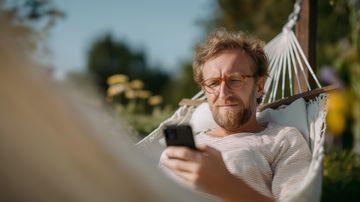 Mann sitzt am Handy in Haengematte